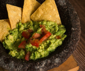 A close-up image of guacamole with tomato chunks served in a stone molcajete with tortilla chips arranged around the edges.